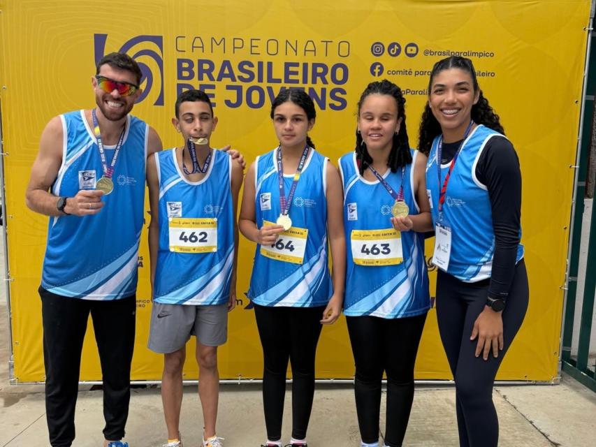 Imagem com os 3 jovens medalhistas, acompanhados dos 2 guias.